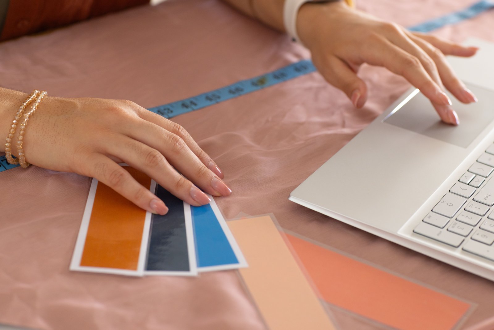 A small business owner holding up paint swatches and fabric samples next to a laptop showing their website, comparing colors in natural light