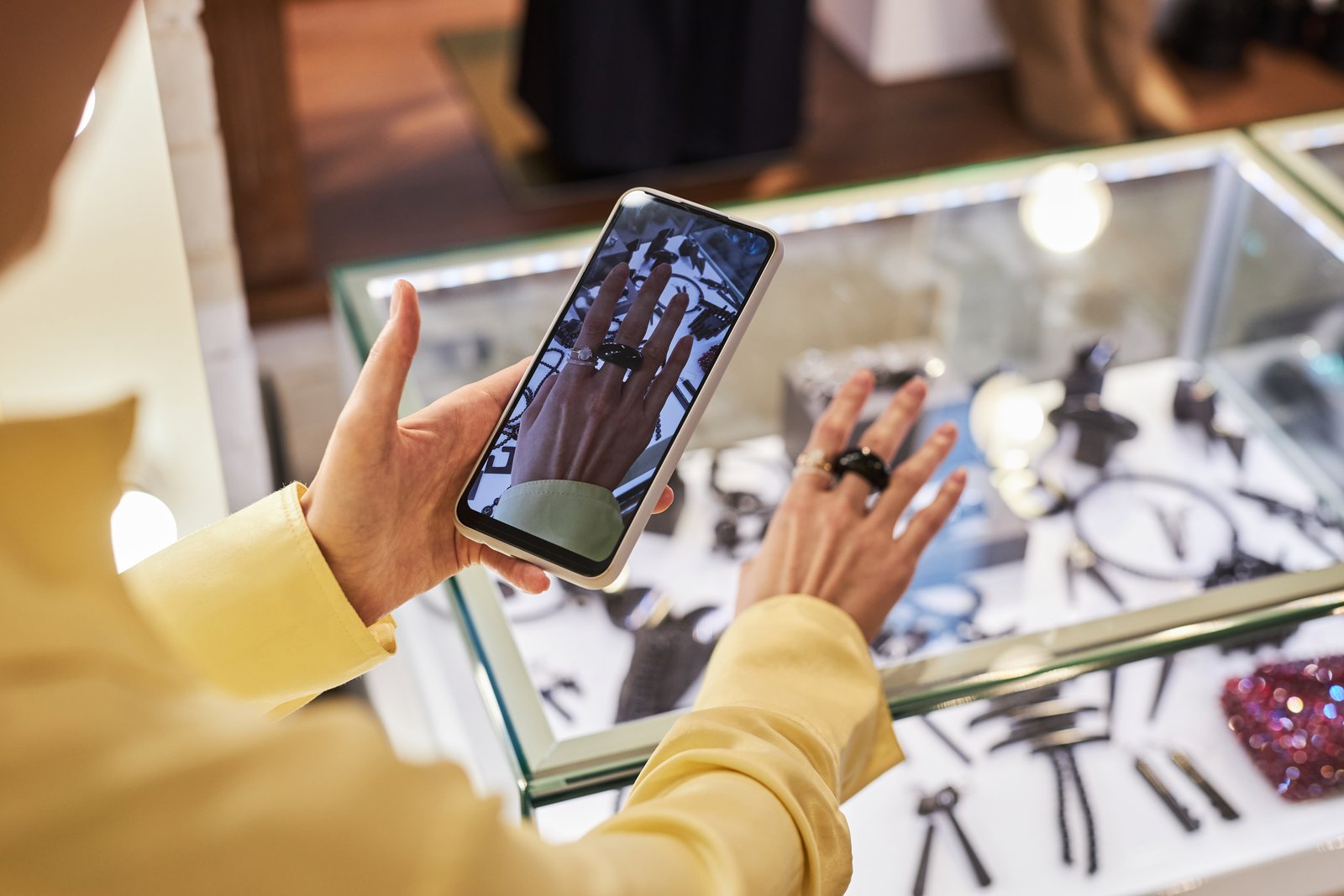 A small business owner holding up a phone to photograph a product on a clean counter near a sunlit window.