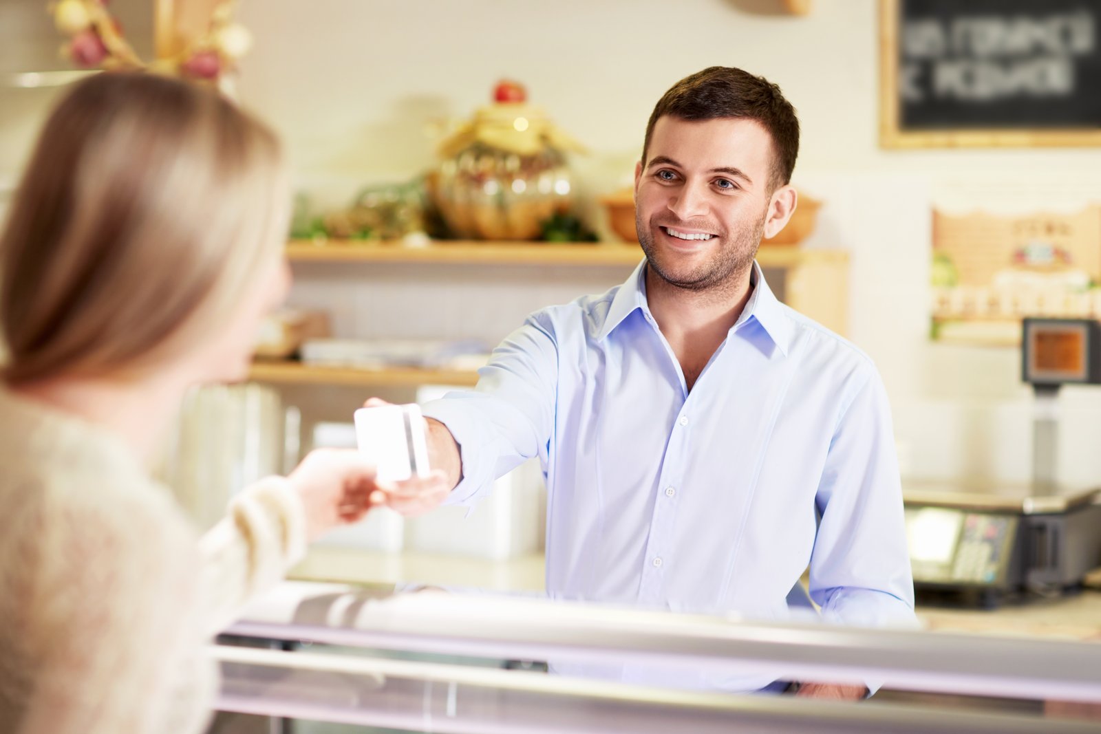 A small business owner handing a simple referral card to a smiling customer at the counter